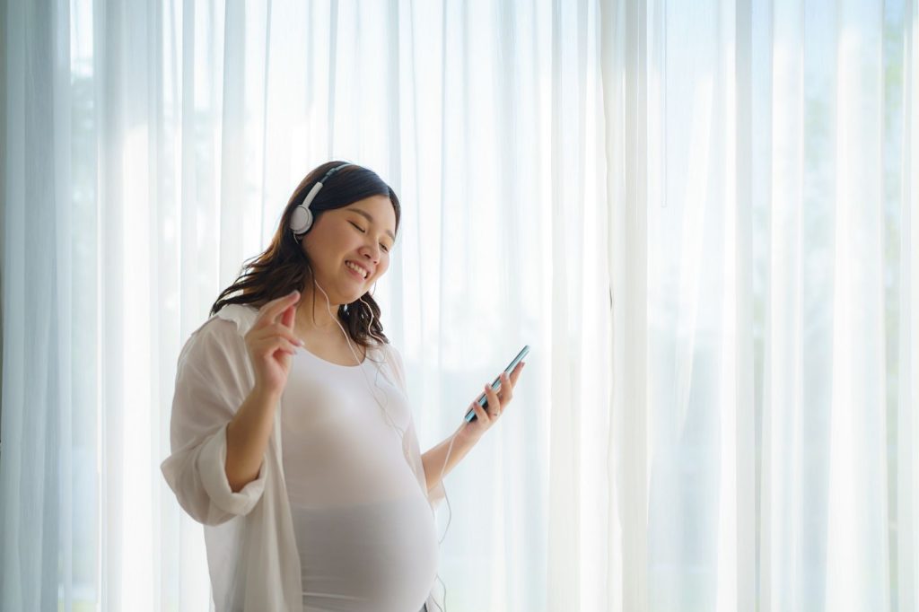 Una mujer embarazada con auriculares y sosteniendo un teléfono.