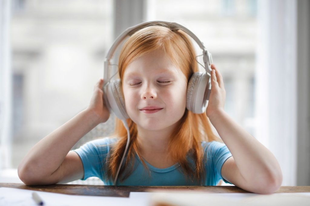 Una niña escuchando música sentada en una mesa.