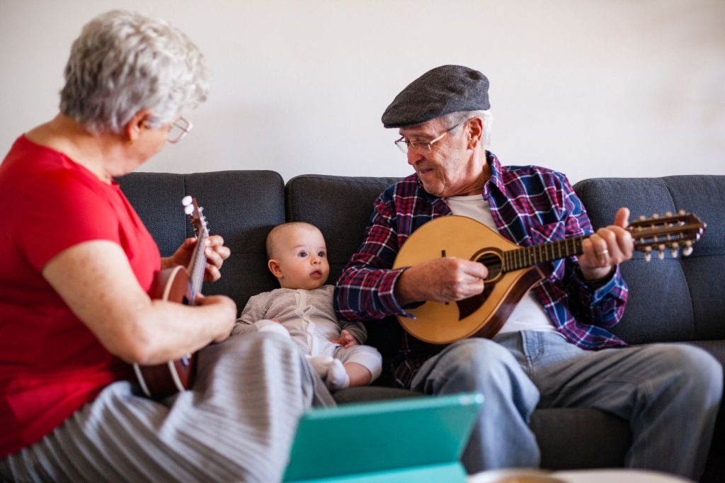 Una pareja de ancianos tocando la guitarra con un bebé sentado en el sofá.